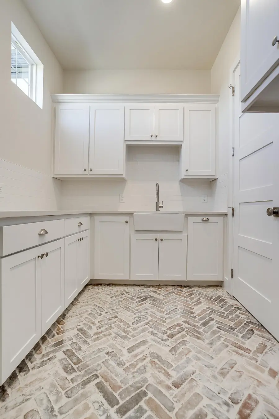 Utility room with farmhouse sink, upper cabinets, and brick floor