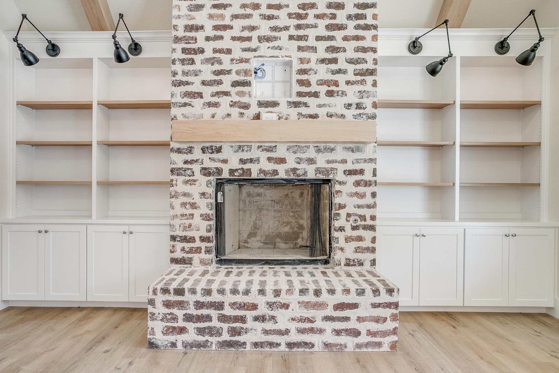 White brick fireplace with a light wood mantel and black sconces