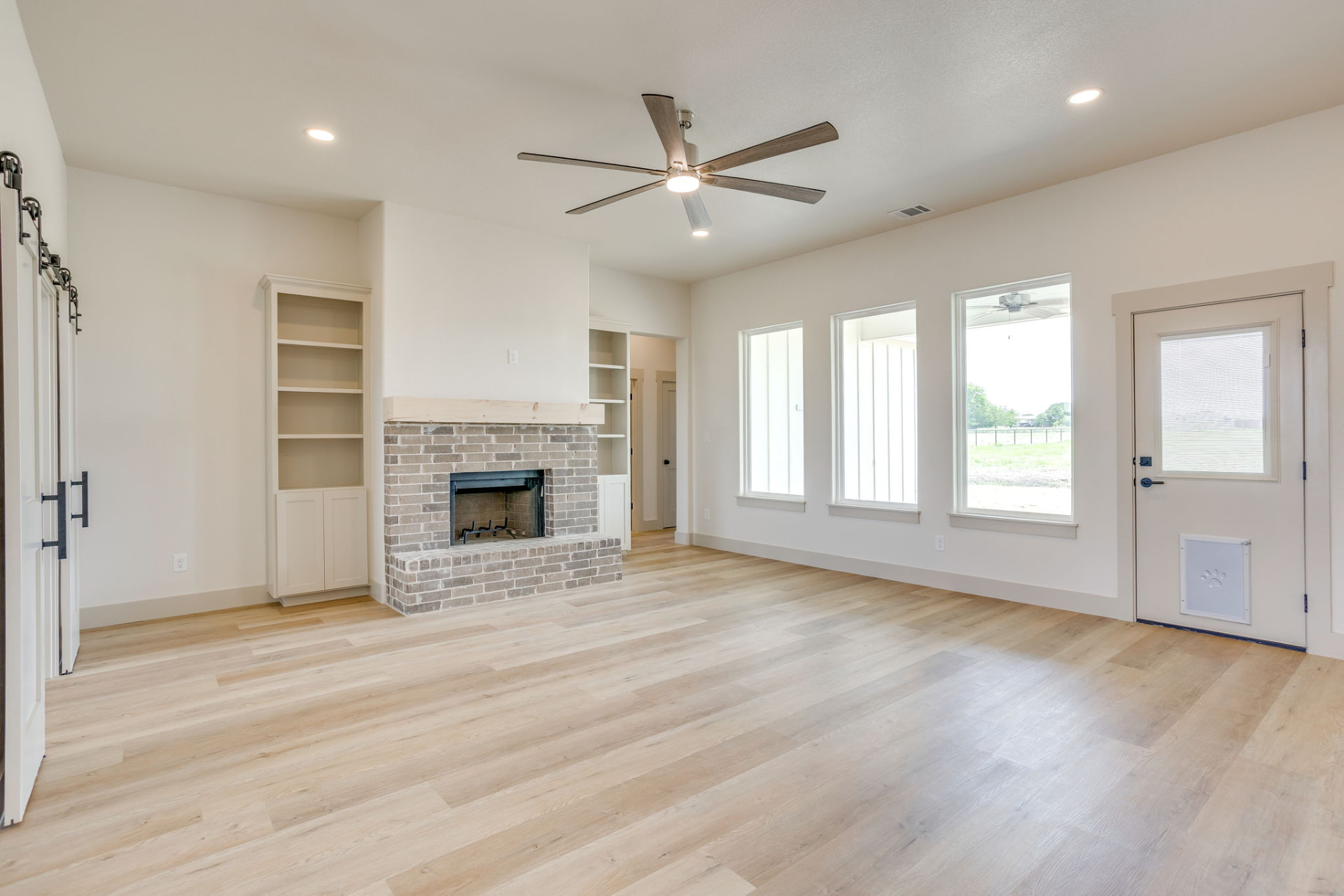Living room with a brick fireplace, wood mantel, and tall windows