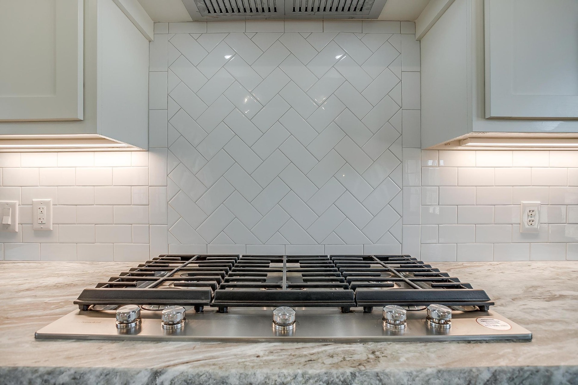 Gas cooktop with white herringbone tile backsplash