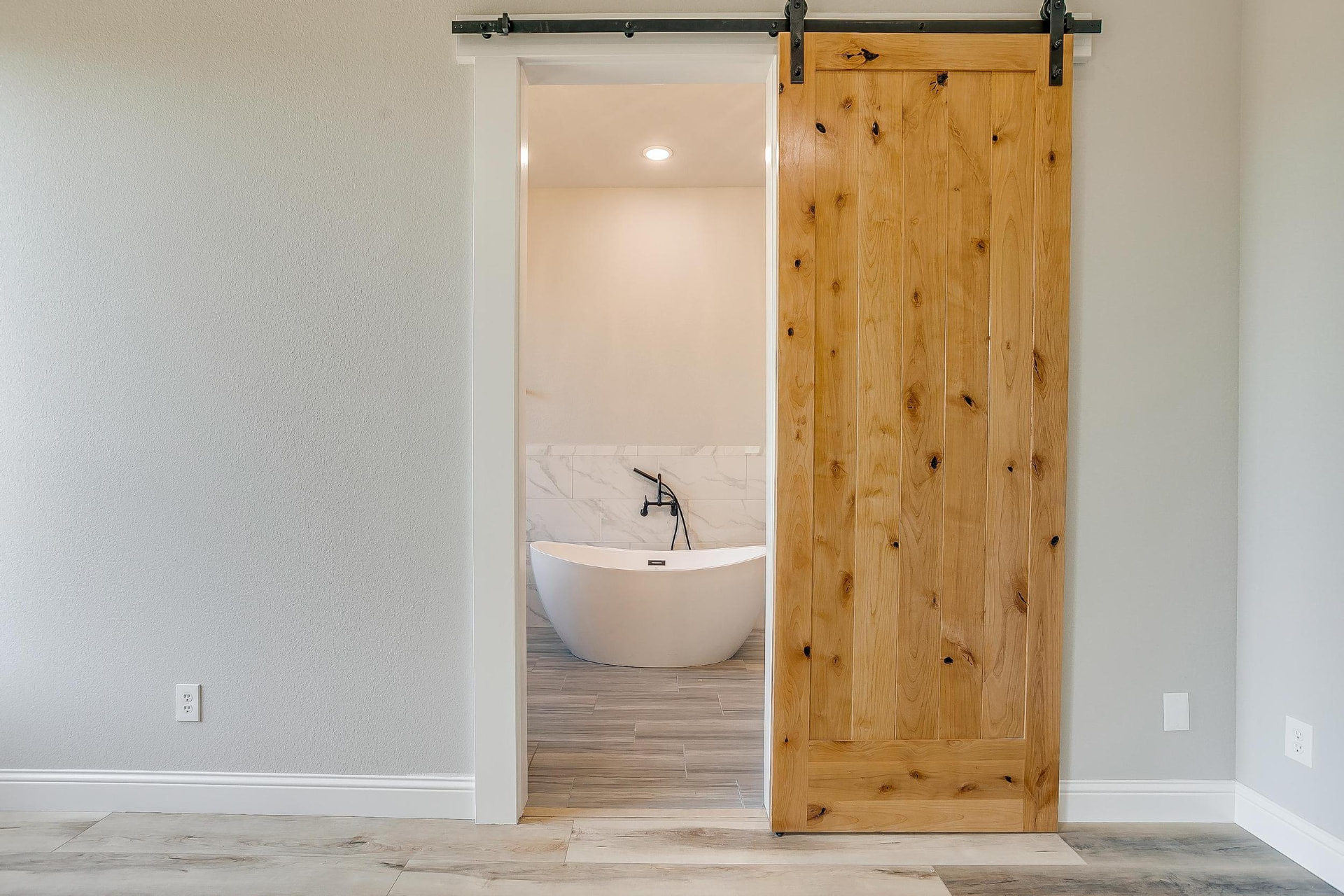 Barn door opening to the primary bath and freestanding soaking tub