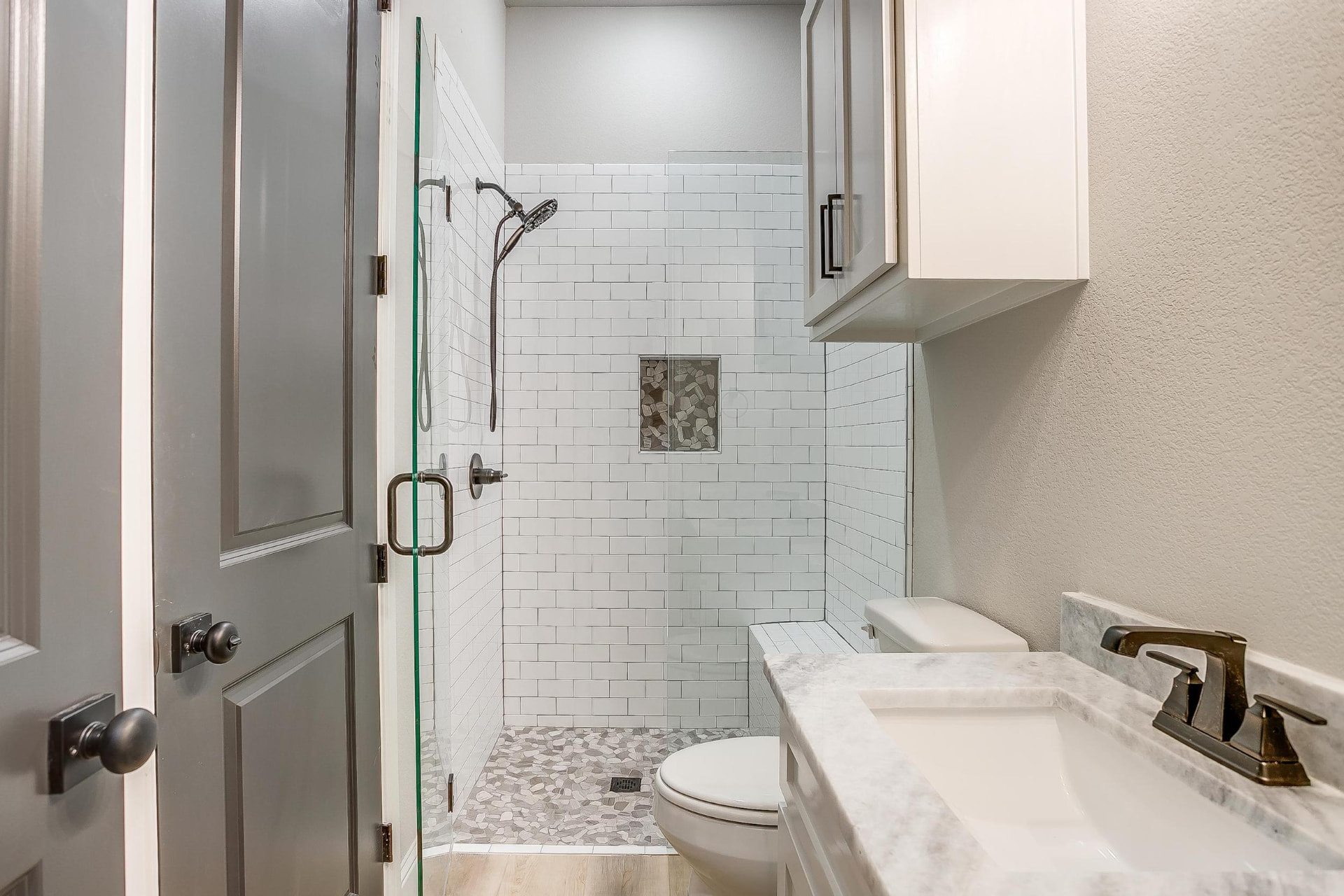 Glass-enclosed shower with white subway tile and pebble floor
