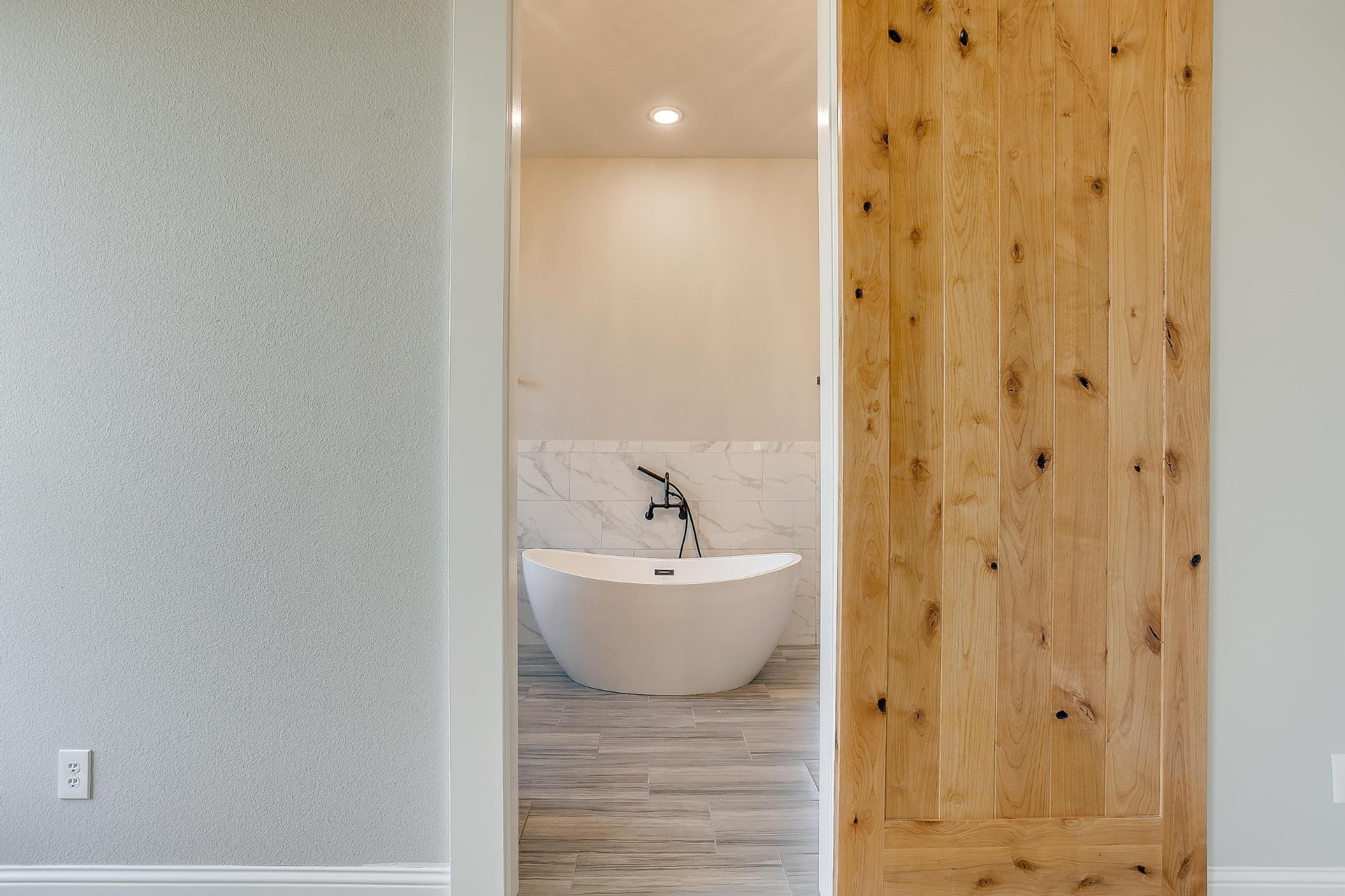 Freestanding soaking tub framed by the primary suite barn door