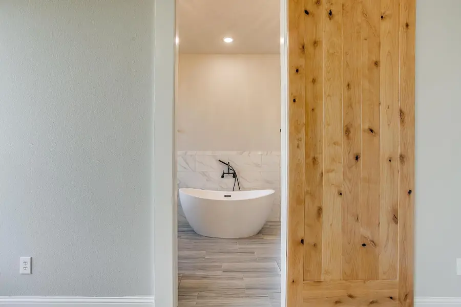Freestanding soaking tub framed by the primary suite barn door