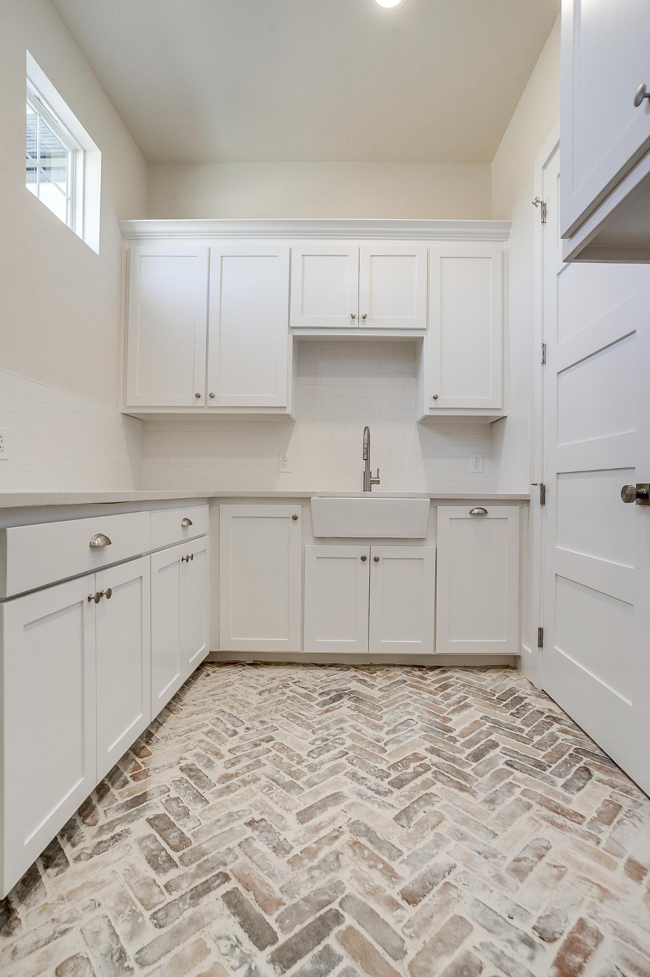 Utility room with farmhouse sink, upper cabinets, and brick floor