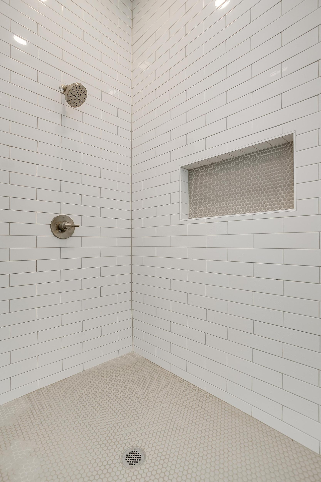 Walk-in shower with vertical subway tile and penny tile floor