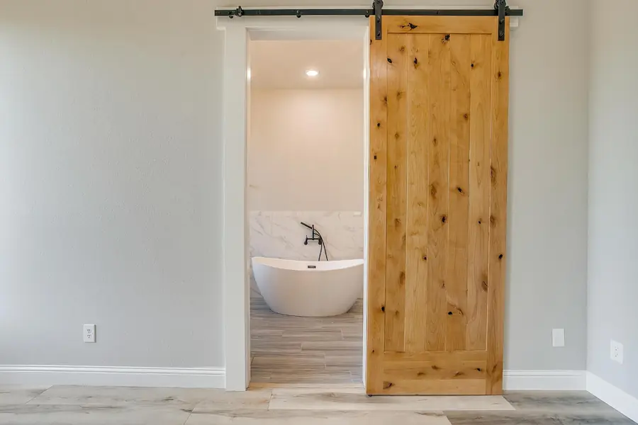 Barn door opening to the primary bath and freestanding soaking tub