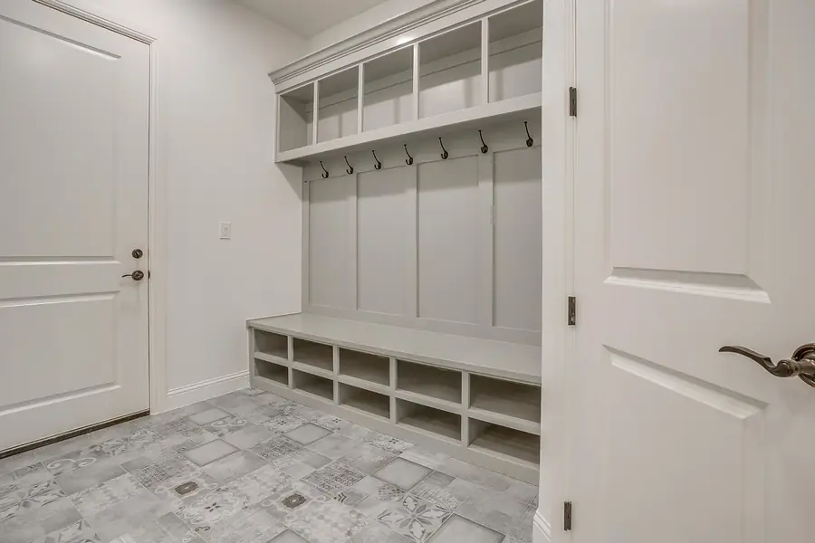 Mudroom with gray built-in bench, hooks, and patterned tile