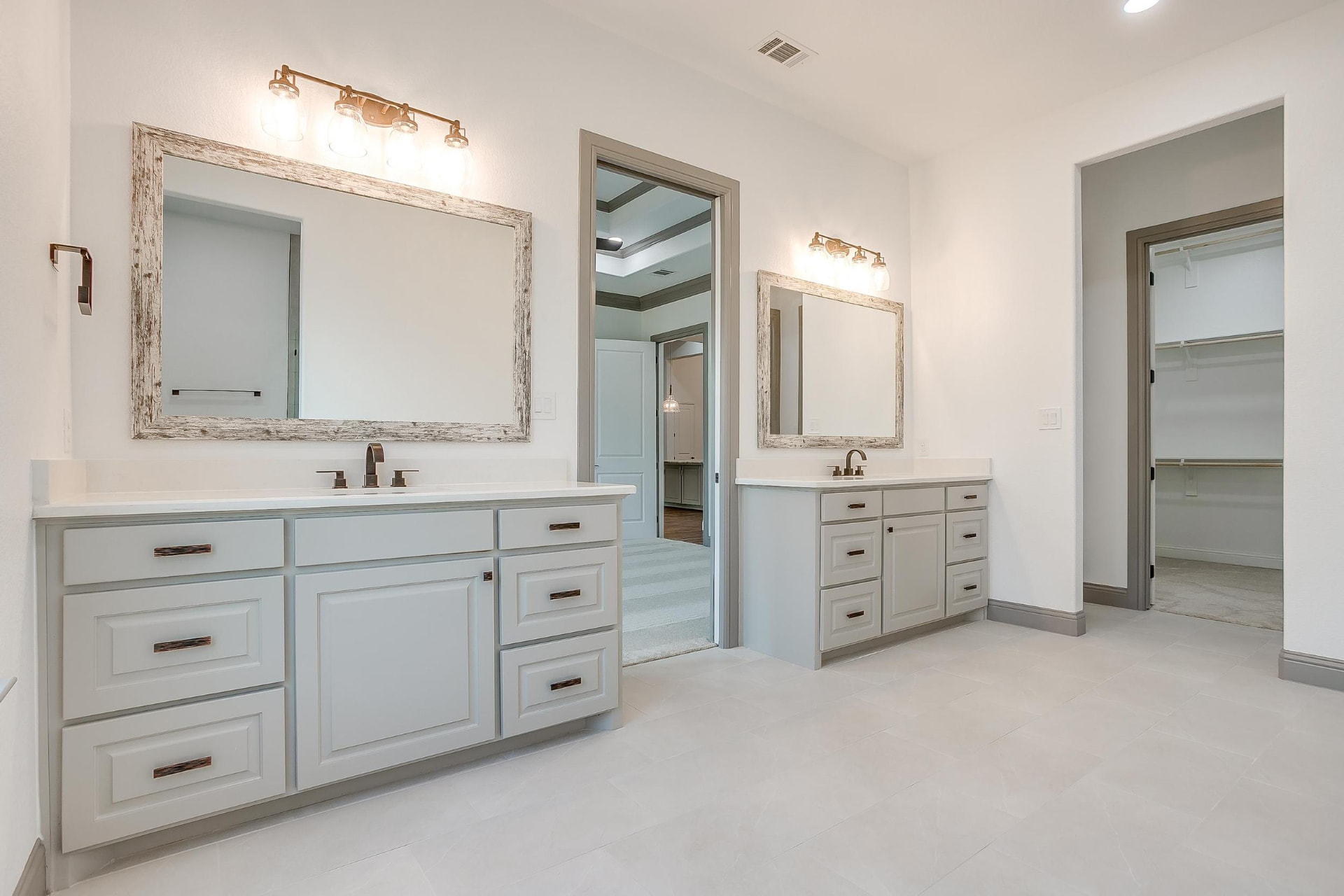 Primary bath with two vanities, walk-in closet, and bedroom beyond