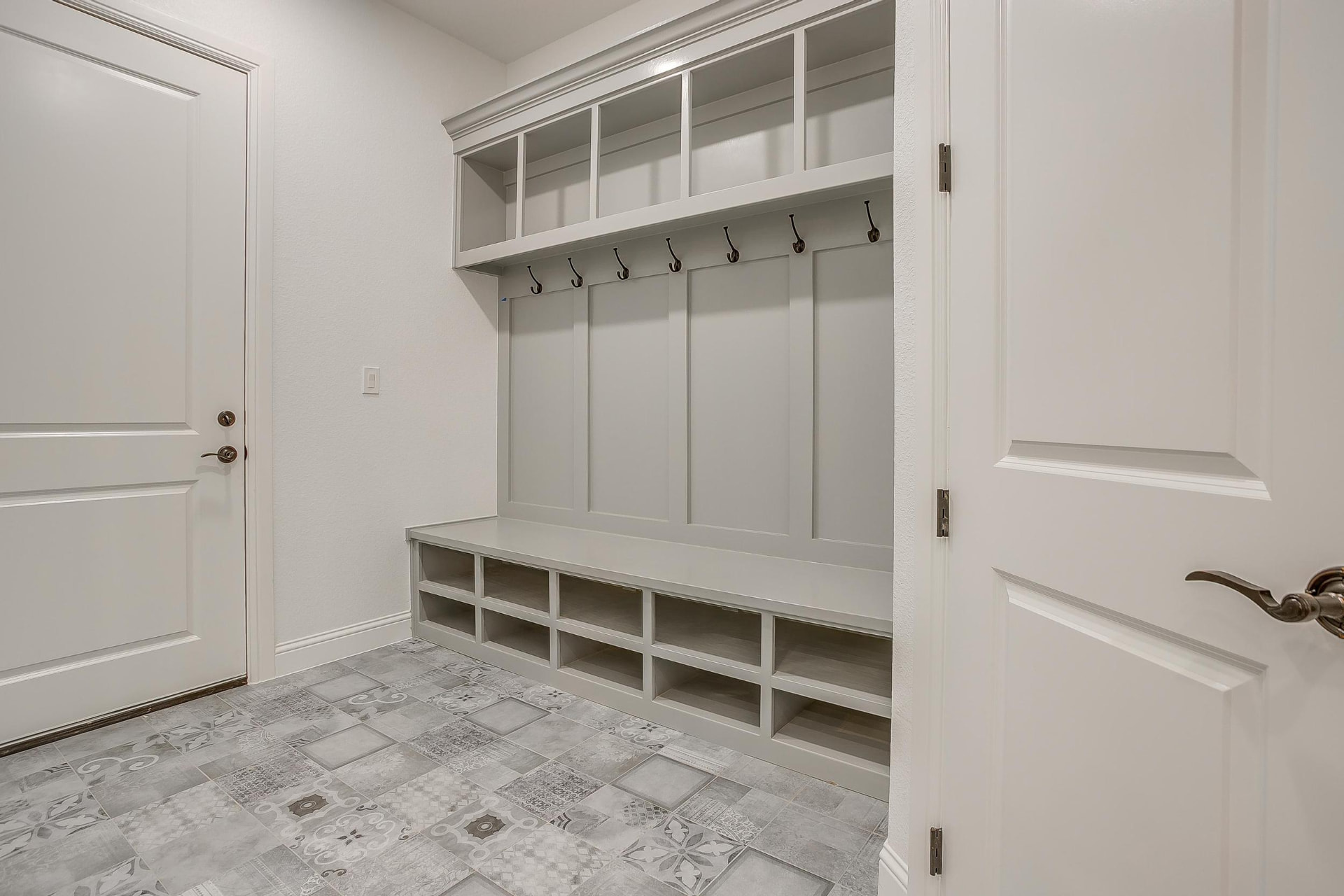 Mudroom with gray built-in bench, hooks, and patterned tile