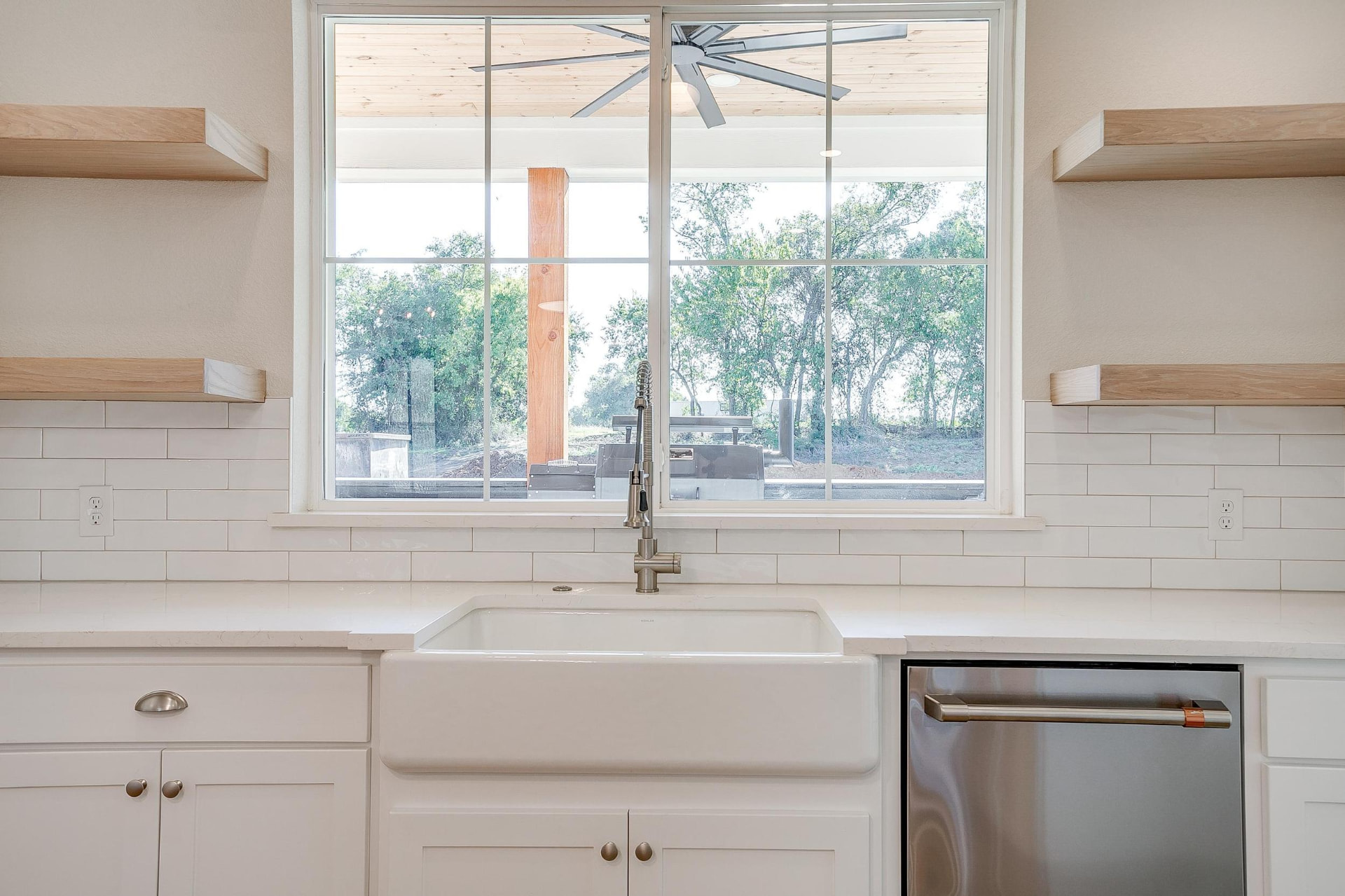Farmhouse sink under a window flanked by wood floating shelves