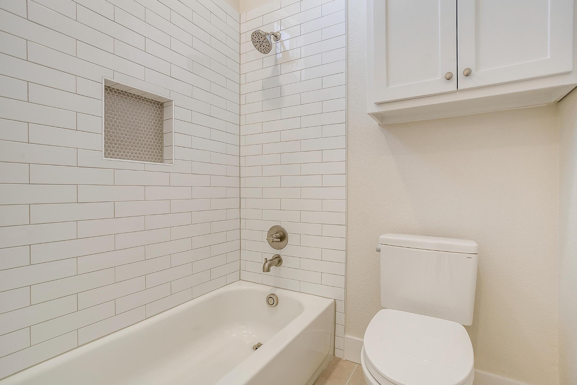 Shower-tub combo with vertical white subway tile and a niche
