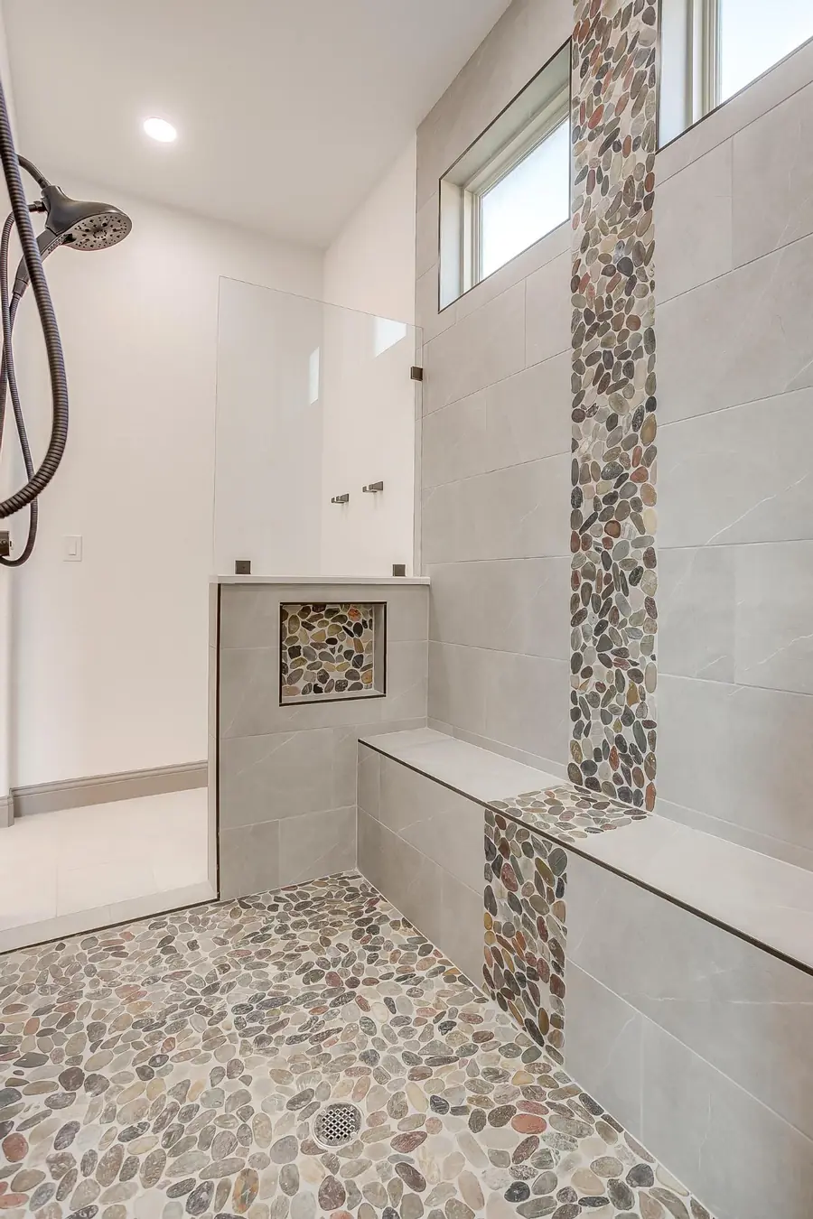 Oversized walk-in shower with pebble mosaic accent column and bench