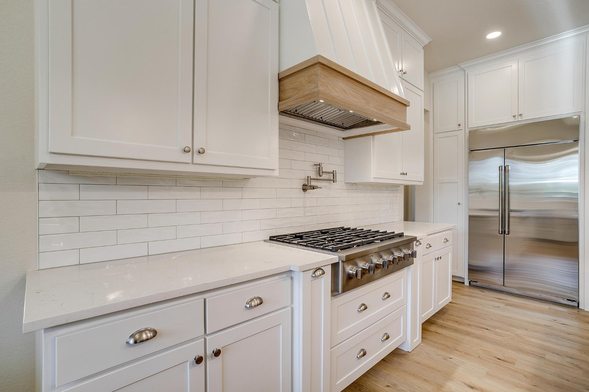 White tile backsplash, gas range, and light wood range hood