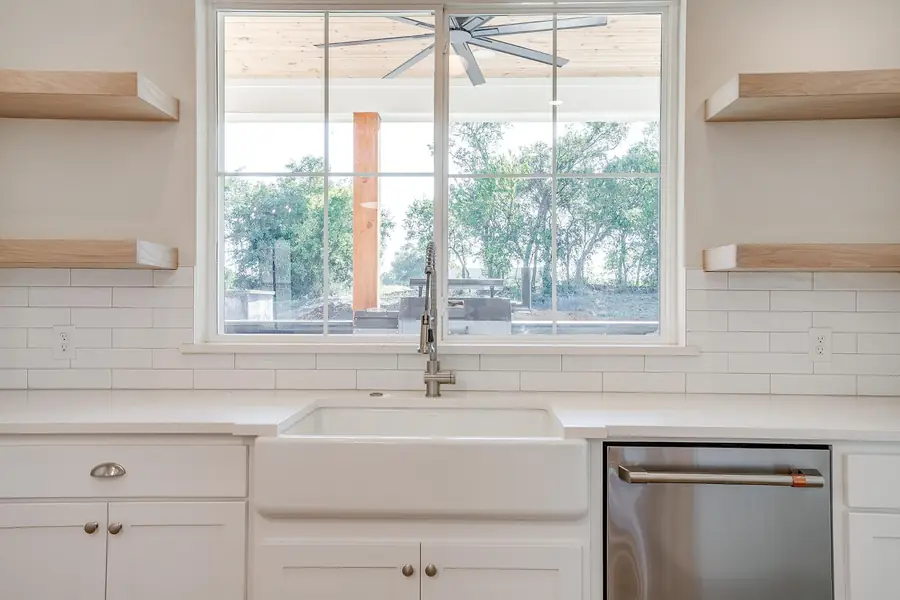 Farmhouse sink under a window flanked by wood floating shelves