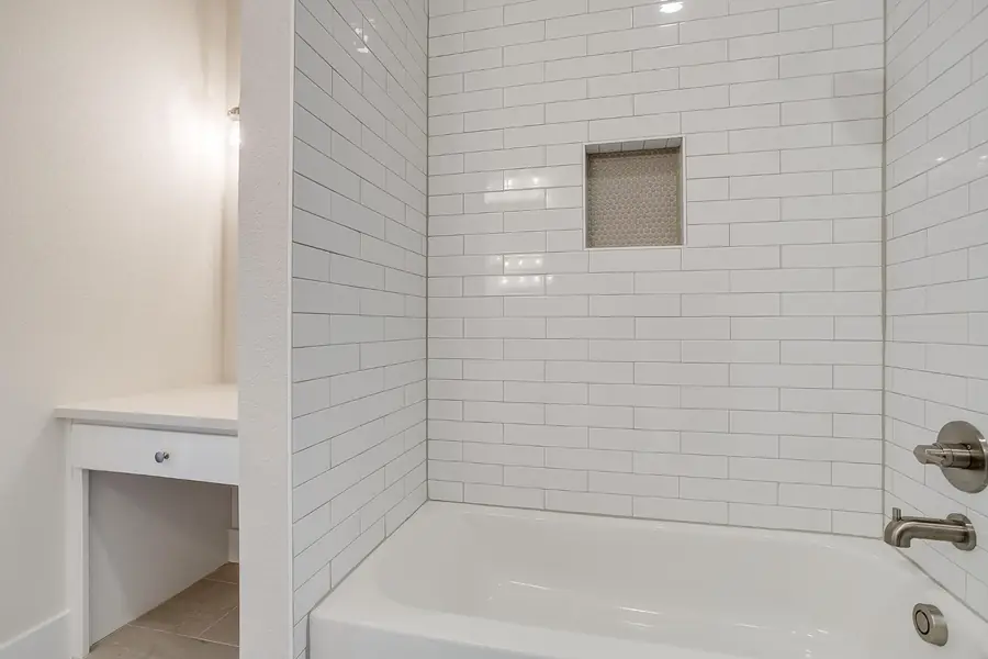 Tub surround in glossy white subway tile with a hex-tile niche