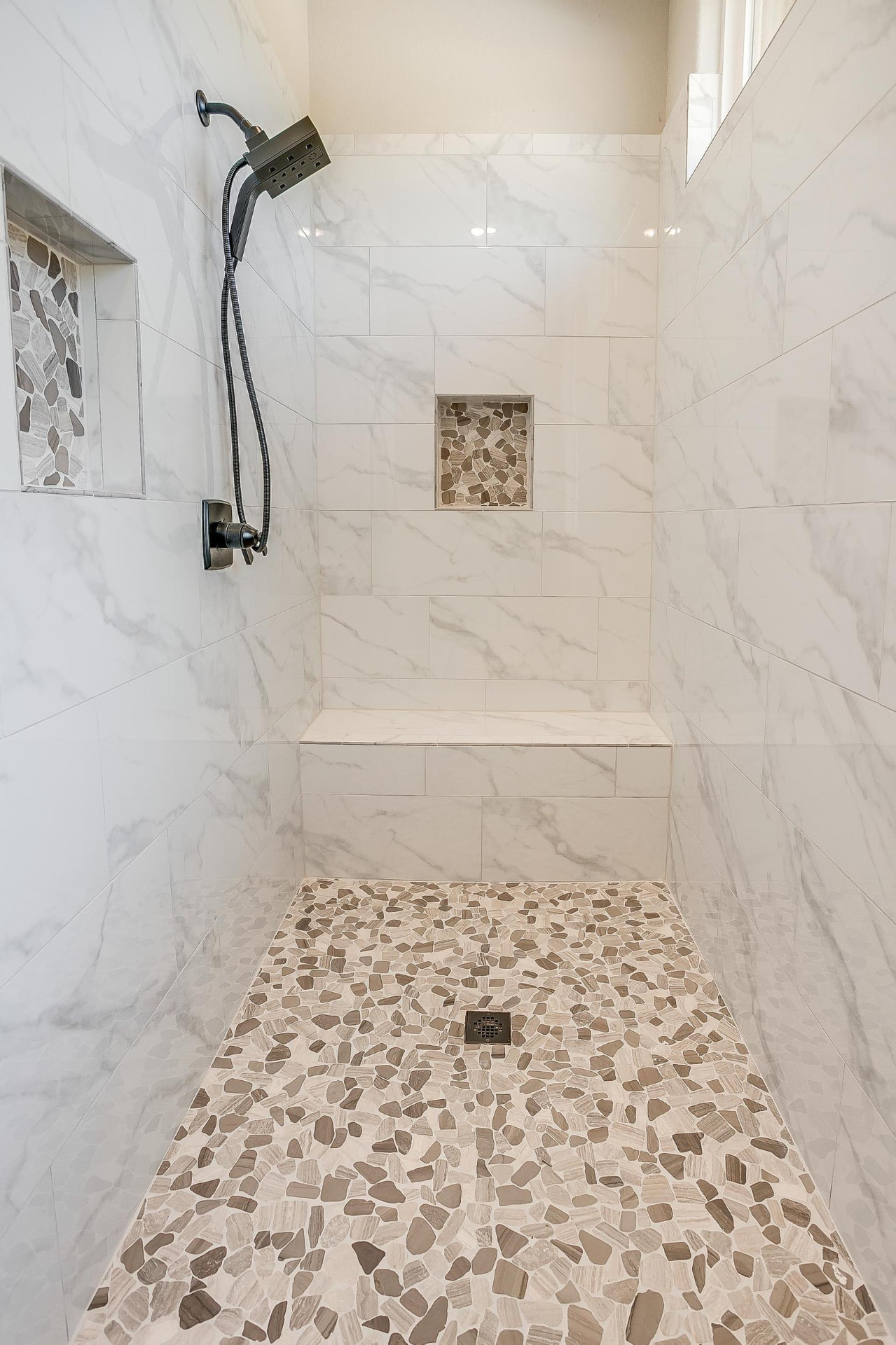 Walk-in shower with pebble floor, bench, and marble tile walls