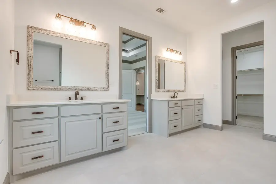 Primary bath with two vanities, walk-in closet, and bedroom beyond