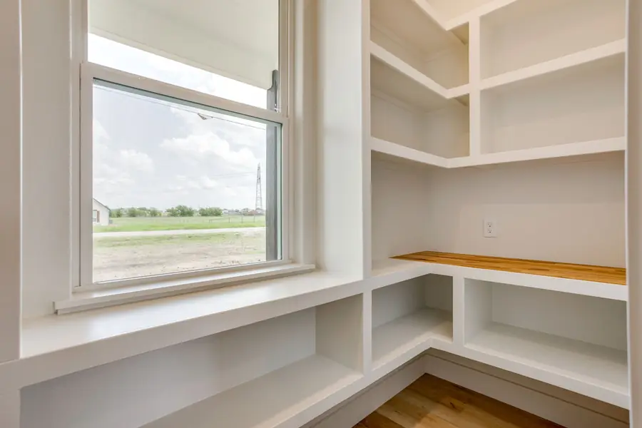 Walk-in pantry with white shelving and a window