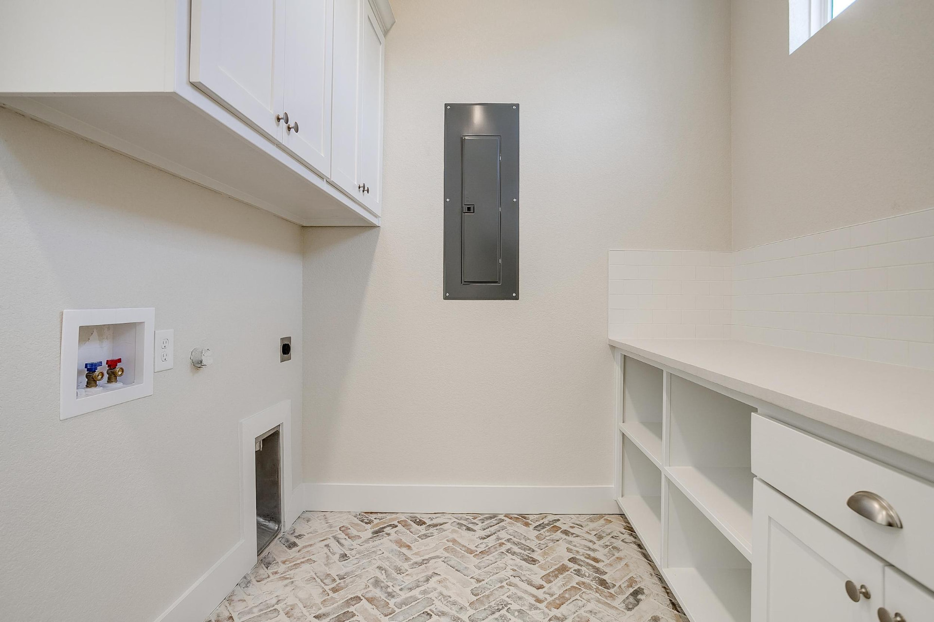 Laundry room with herringbone brick floors and white cabinetry