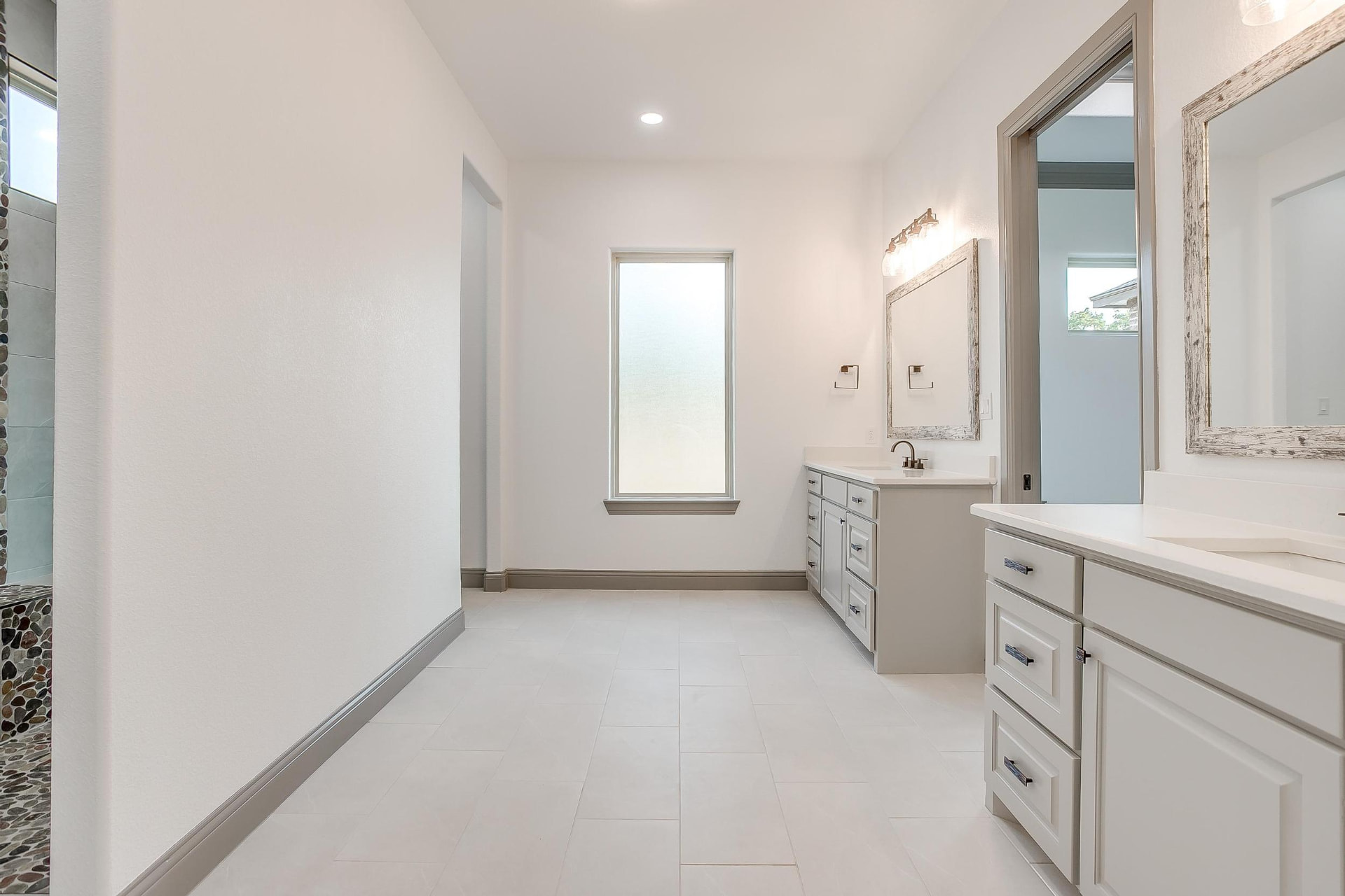 Primary bathroom with light tile flooring and dual vanities