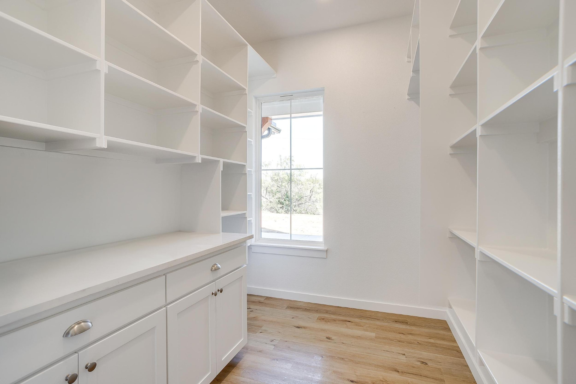 Walk-in primary closet with custom white shelving and a window