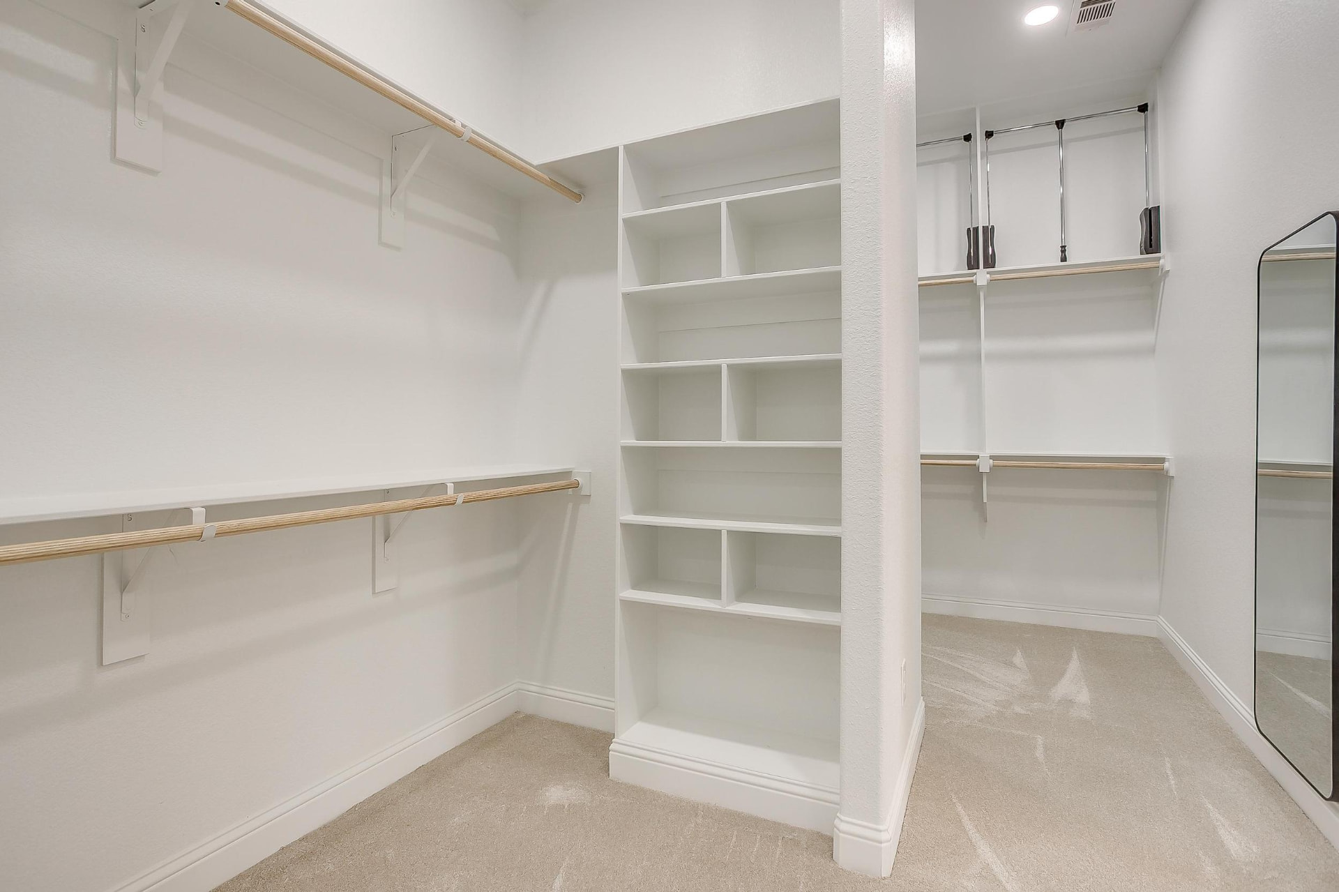 Walk-in primary closet with built-in shelving and hanging rods
