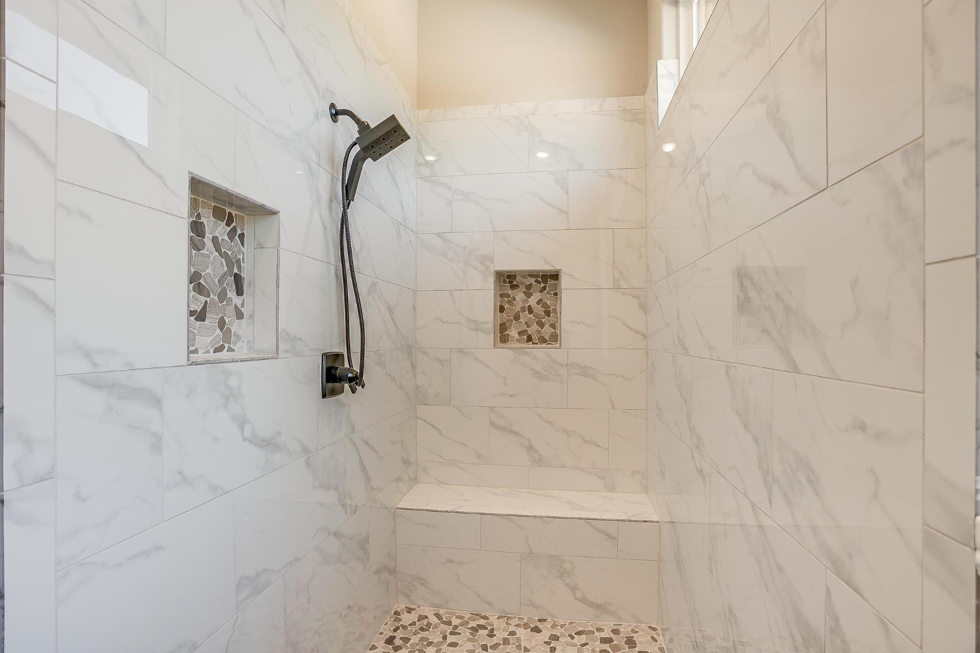 Marble tile walk-in shower with pebble niches and bench
