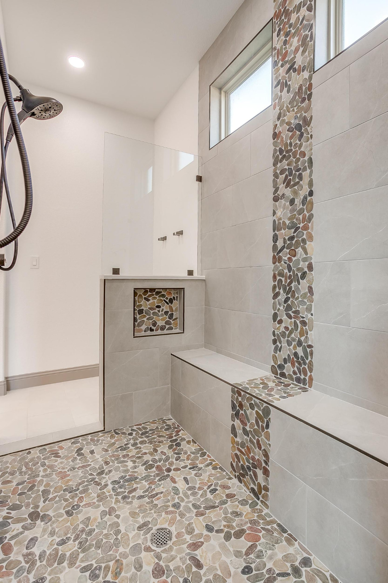 Oversized walk-in shower with pebble mosaic accent column and bench