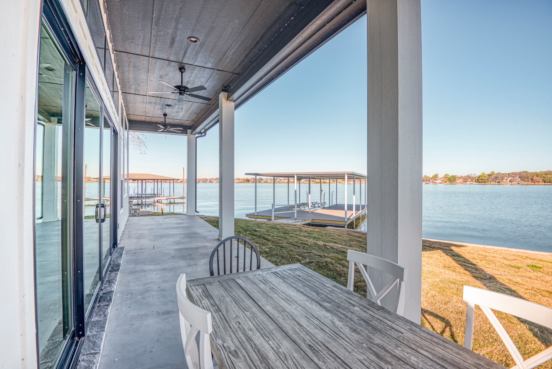 Covered concrete back patio looking out to the lake and boat dock