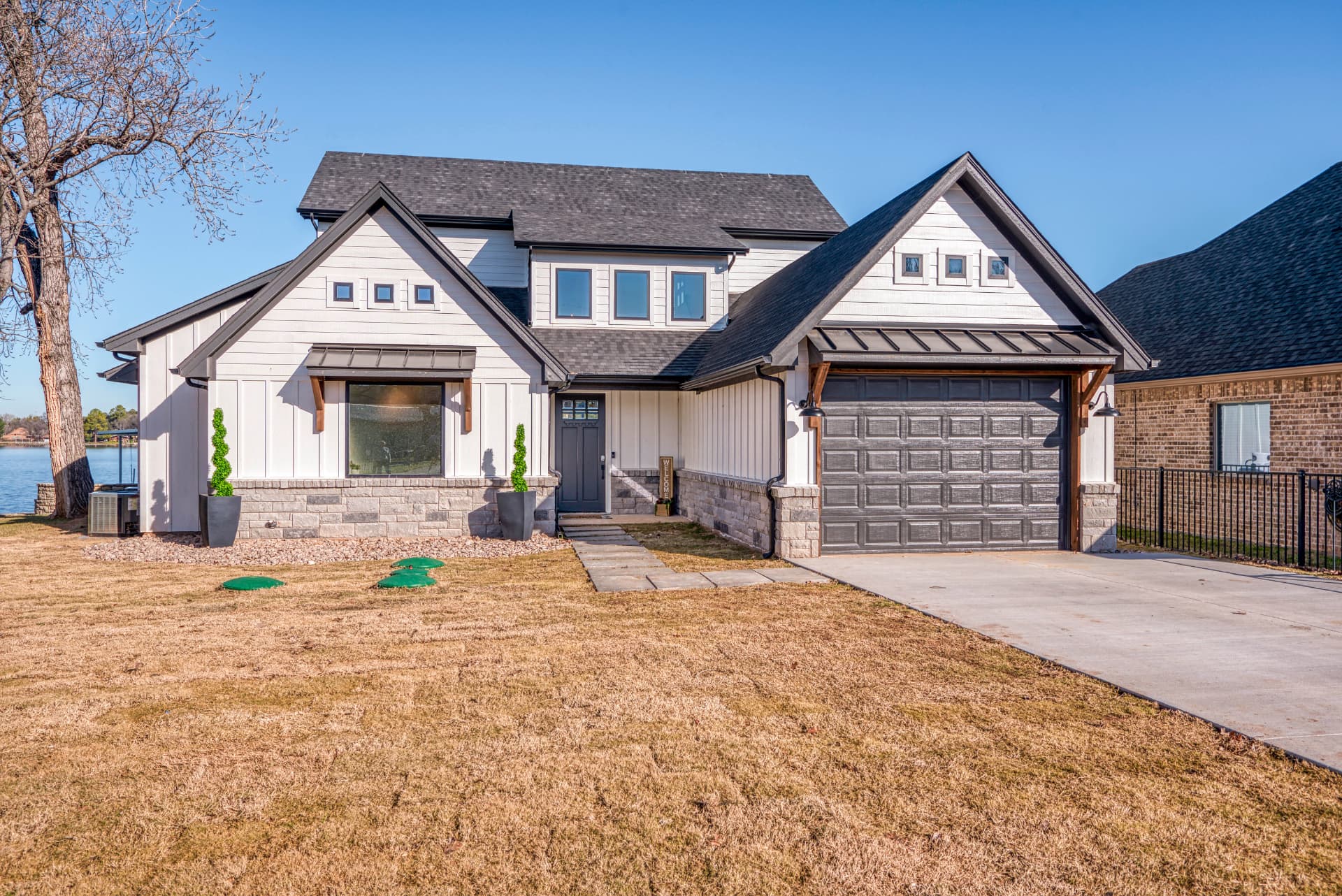 Front exterior of a modern white farmhouse with black gables and stone wainscoting