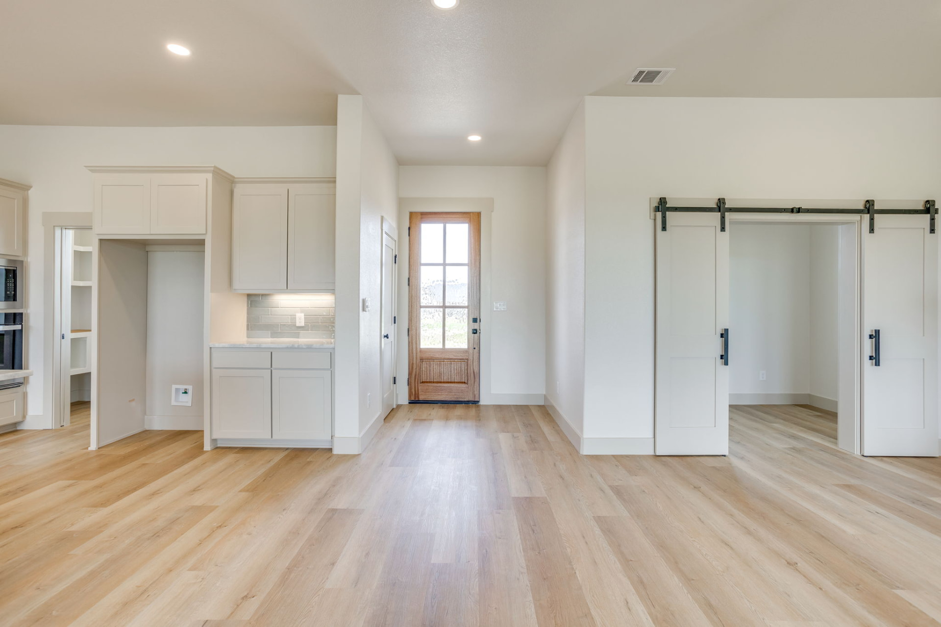 Entry foyer with light wood floors and white barn doors to the front office