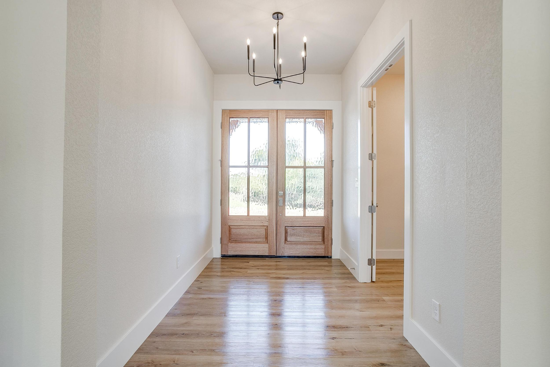 Entry foyer seen through the wood front door with a black chandelier