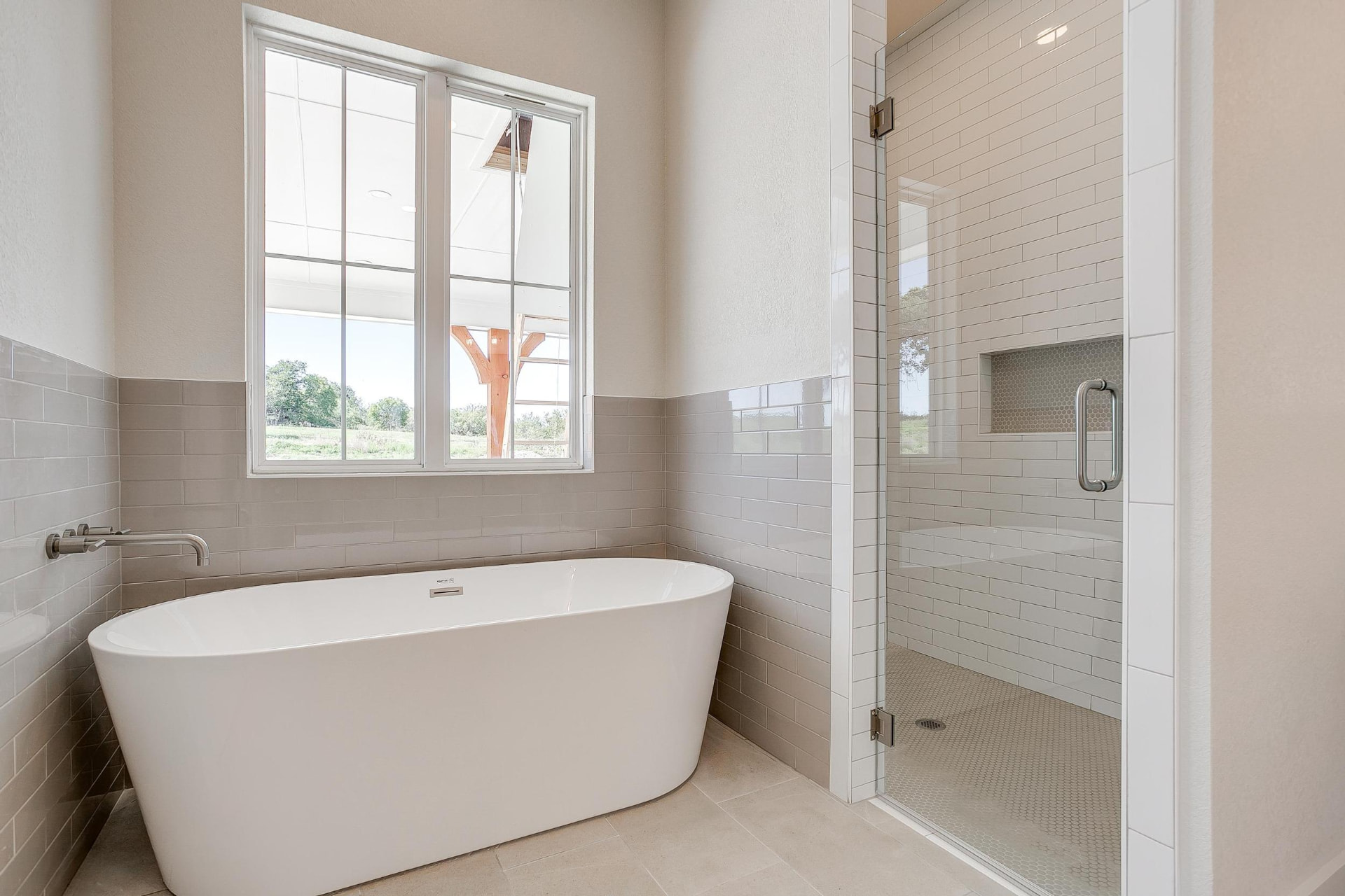 Freestanding soaking tub against a taupe tiled wall