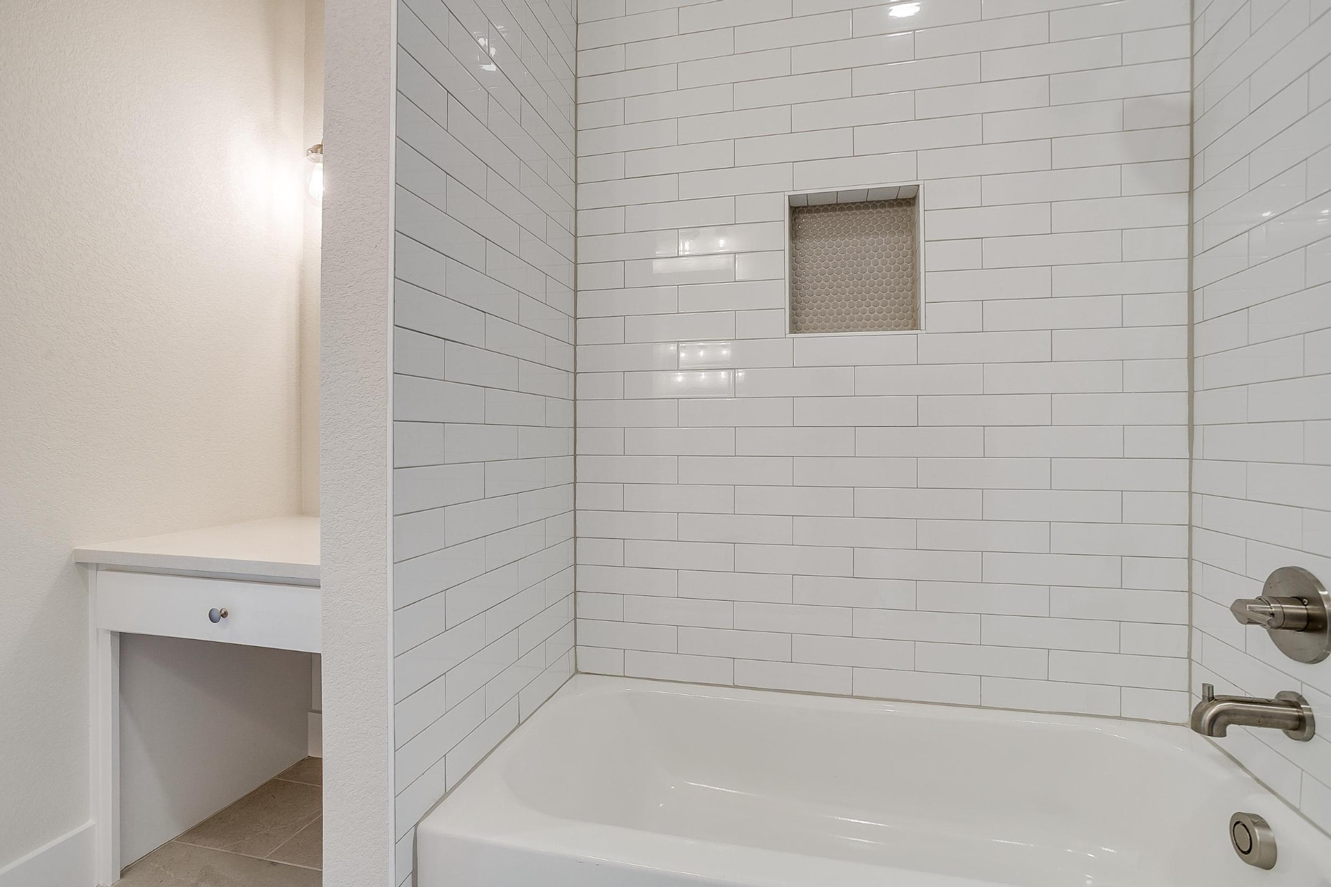 Tub surround in glossy white subway tile with a hex-tile niche